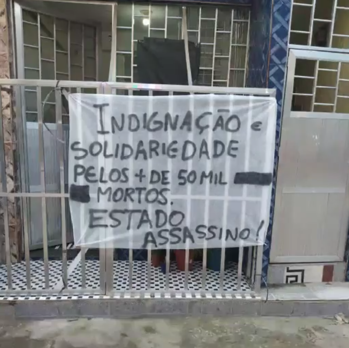 Faixa amarrada em portão com os dizeres: Indignação e solidariedade pelos mais de 50 mil mortos. Estado Assassino!